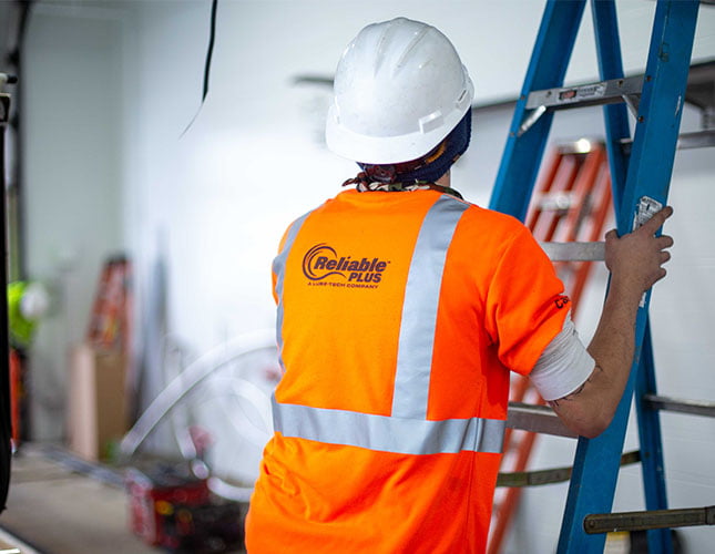 Reliable Plus technician about to climb a ladder